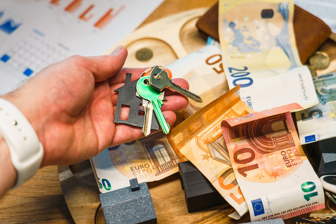 House keys euro banknotes real estate investment concept with symbolic keychain in hand, surrounded by money and financial charts on wooden desk