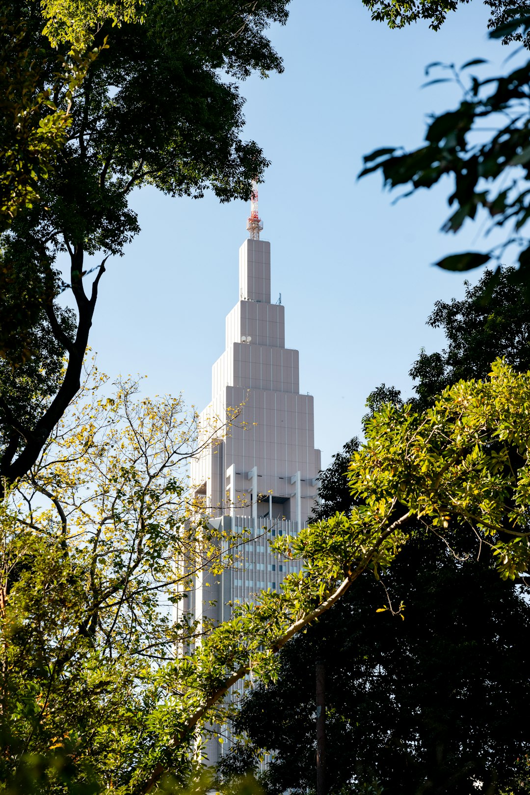 skyscraper-seen-through-green-trees-against-blue-sky-e4r3ye7vyym